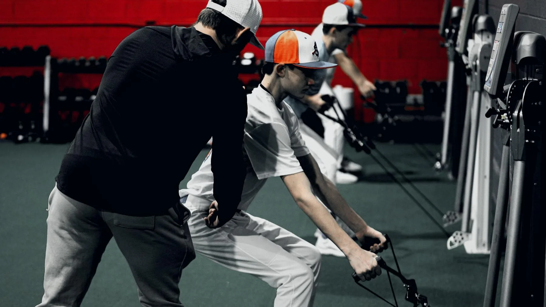 Garrett coaching an athlete through a rep on the Keiser pneumatic trainers at GPS Performance Training, with two more athletes working on adjacent units.