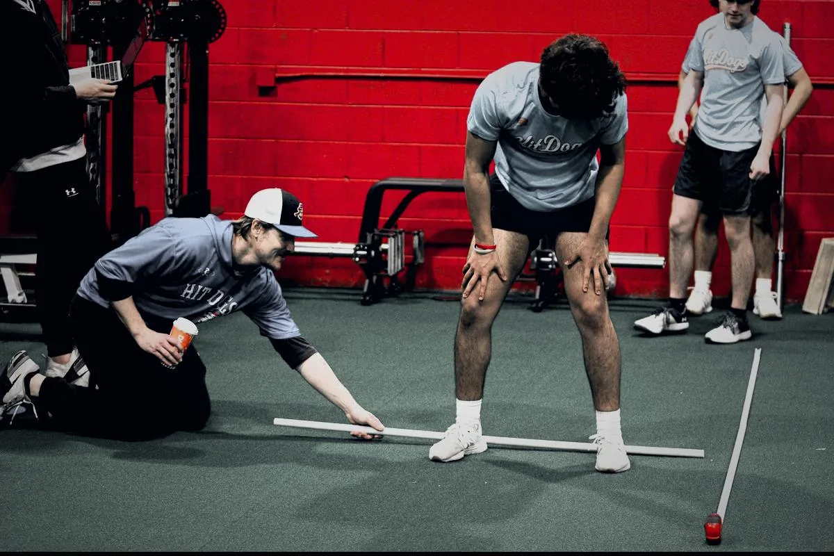 A GPS coach measuring an athlete's broad jump distance with a tape on the turf